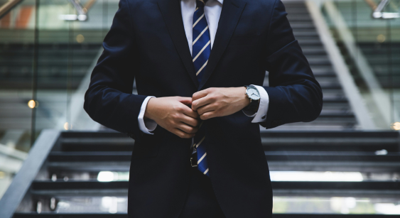 Professionnel en costume bleu ajustant sa veste dans un environnement d'entreprise moderne avec escalier en arrière-plan.